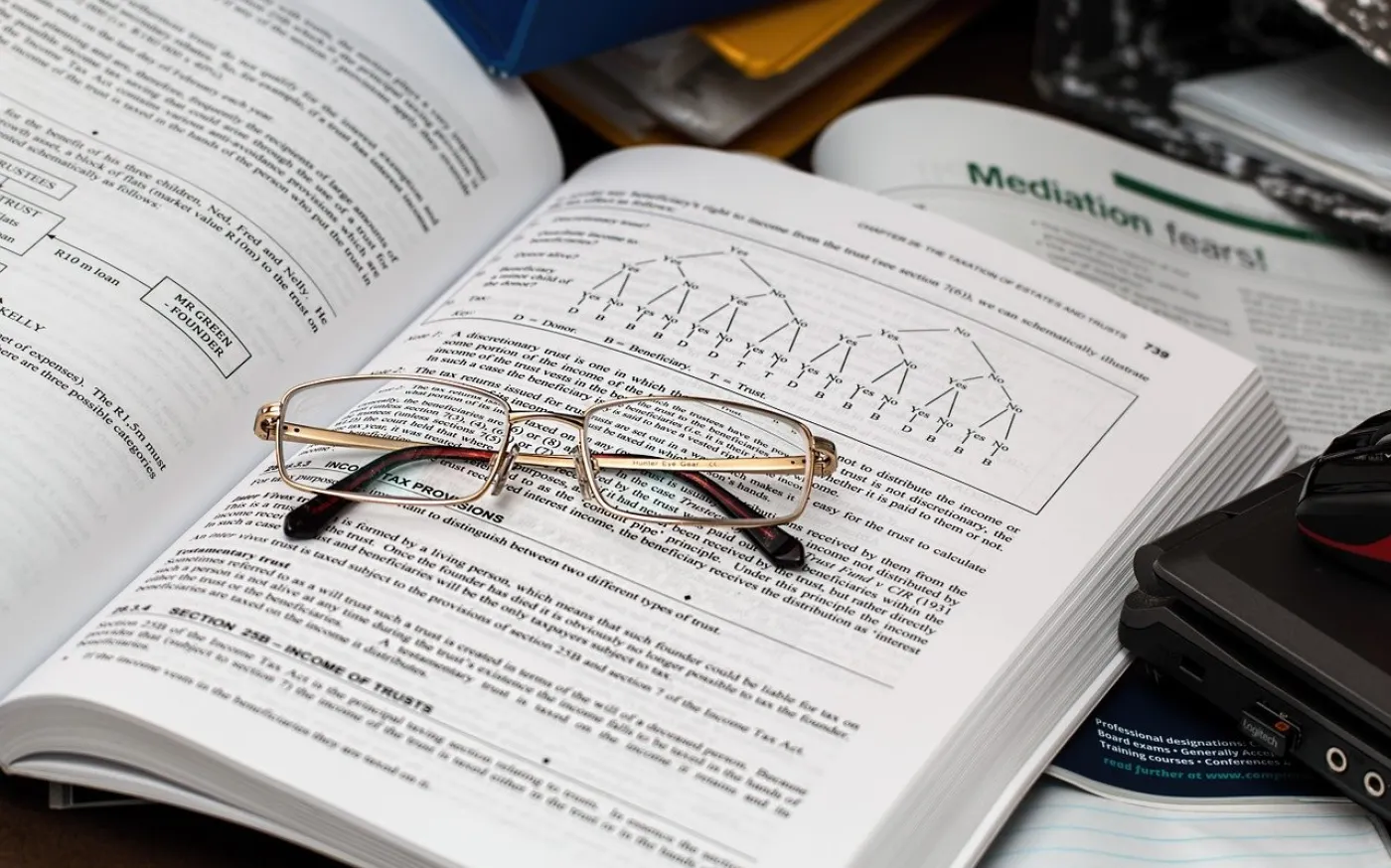 A pair of reading glasses sitting on an open textbook. The book has content on taxes.